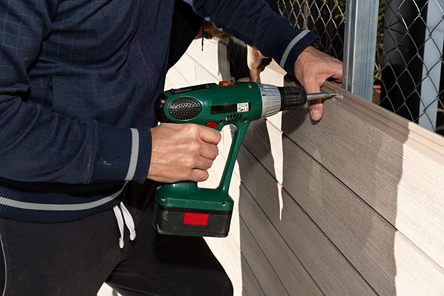 a person using a drill to drill into a composite fence.